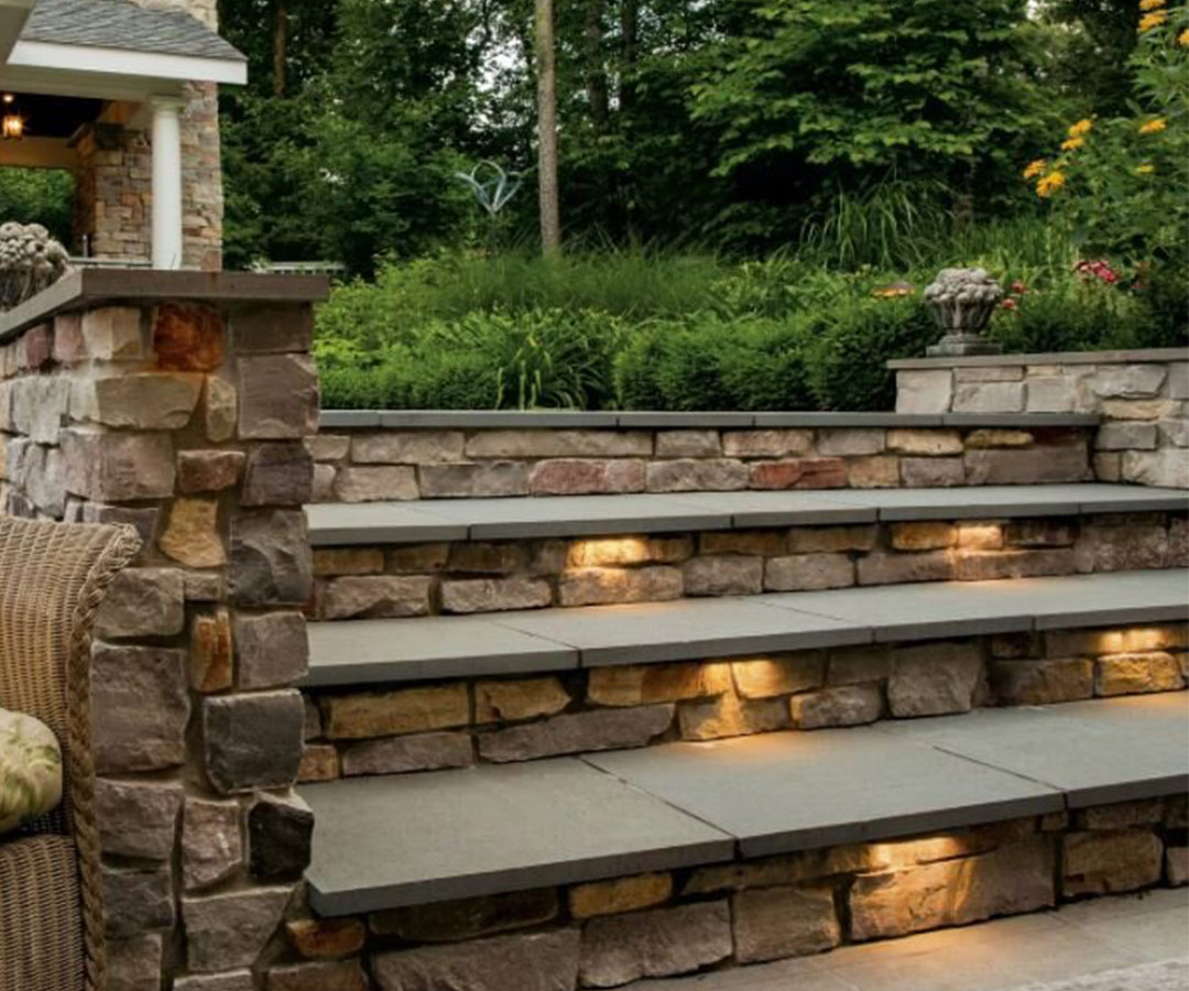 Stair lighting is featured on a natural stone staircase in a Landscape design created by Helios