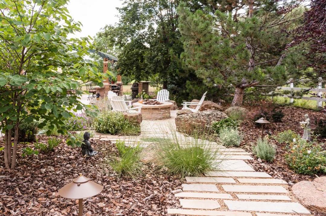 A beautiful and natural path amidst some xeric plants leads to a fire pit with Adirondack chairs put together by a landscaper design - Kristen Whitehead from Helios Landscape Design
