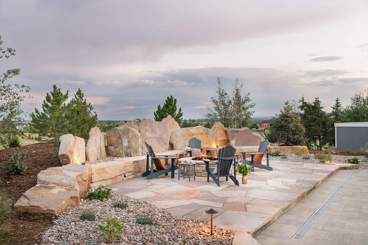 Patio table nestled into a rock patio that is backed by larger boulders and a surrounding landscape design.