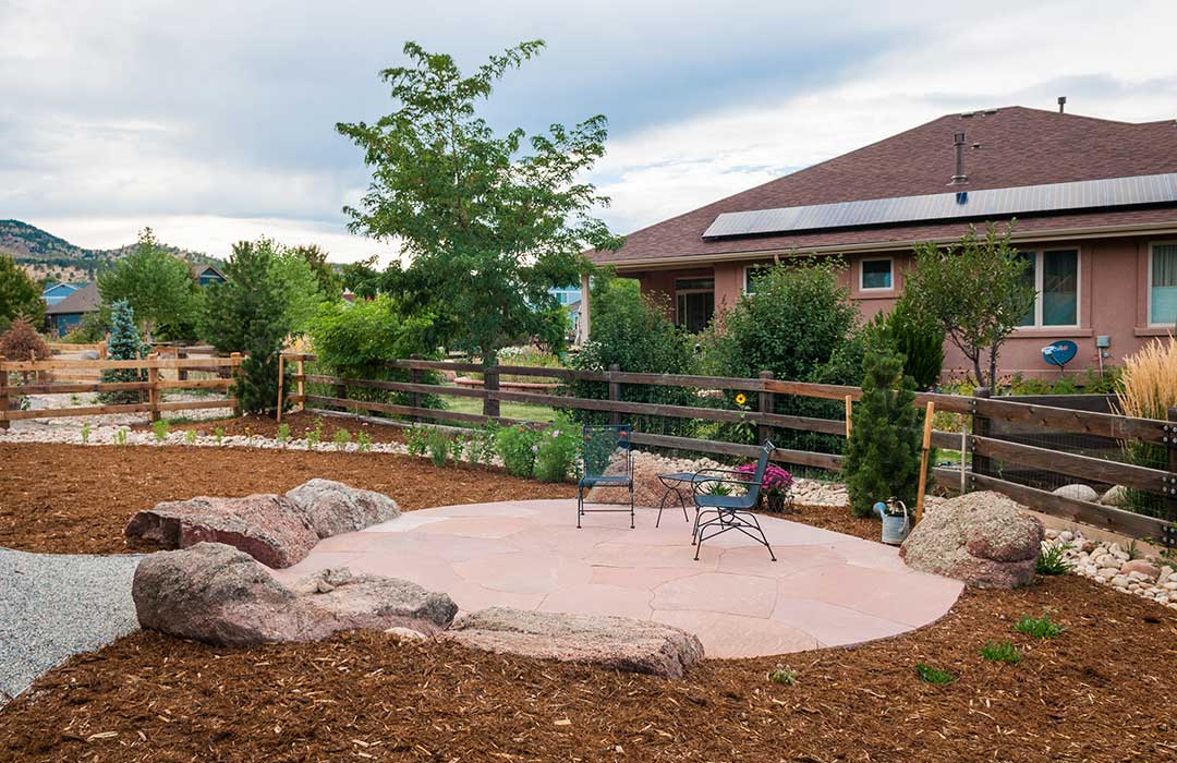 A clean lawn alternative for colorado is shown using a flagstone patio surrounded by moss rock and mulch with new plants. 